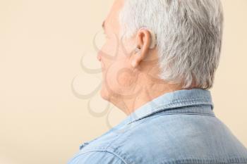 Mature man with hearing aid on light background�
