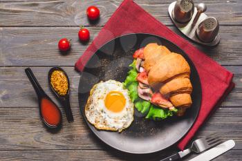 Plate with tasty croissant sandwich and fried egg on table�