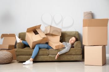 Sleeping woman with heap of moving boxes lying on sofa in new house�