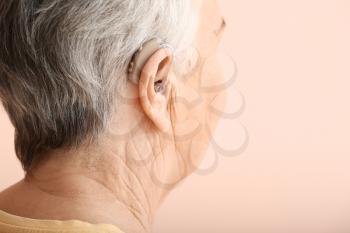 Senior woman with hearing aid on color background, closeup�