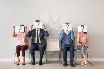 Young people holding paper sheets with question marks while sitting on chairs indoors. Job interview concept�