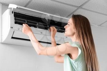 Young woman cleaning air conditioner at home�