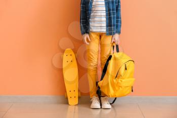 Cute little boy with skate and backpack near color wall�