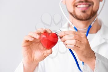 Male cardiologist with red heart on light background, closeup�