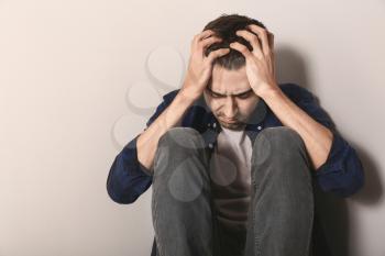 Depressed young man sitting near light wall�