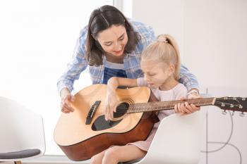 Private music teacher giving guitar lessons to little girl at home�