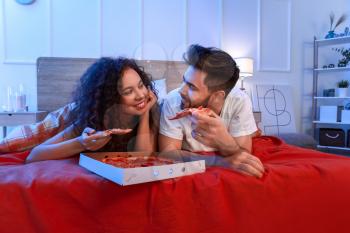 Happy young couple eating pizza in bedroom�