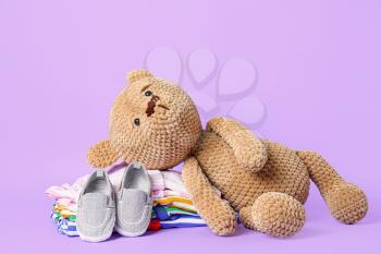 Teddy bear with baby clothes on color background�