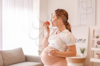 Beautiful pregnant woman with water and apple at home�