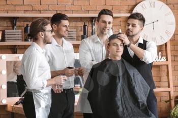 Professional hairdresser teaching young men in salon�