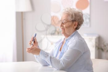 Diabetic senior woman measuring blood sugar level at home�