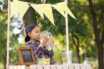 Little African-American boy drinking natural lemonade at stand in park�