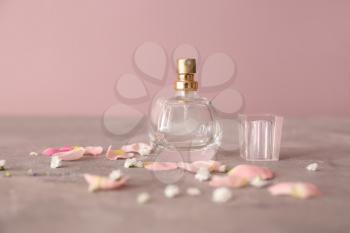 Bottle of perfume with flower petals on grey table�