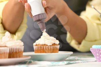 Woman decorating delicious cupcake with cream at table, closeup�