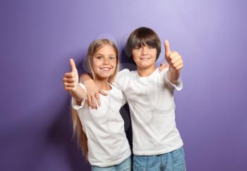 Hugging boy and girl in t-shirts showing thumb-up on color background�