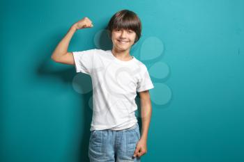 Little boy in t-shirt showing muscles on color background�