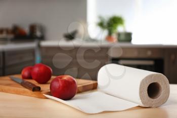 Roll of paper towels with apples and cutting board on kitchen table�