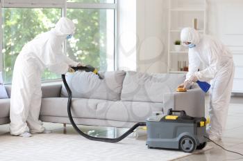 Workers in biohazard costume removing dirt from sofa in house�