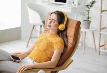 Sleepy young woman listening to music at home�
