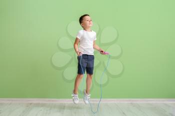 Cute little boy jumping rope near color wall�