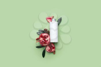 Composition with bottle of cosmetic product and pomegranate on color background�