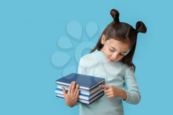 Cute little girl with books on color background�