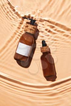 Bottles of cosmetic products in water on color background�