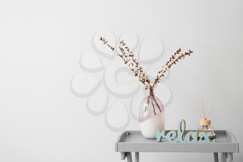 Vase with blooming spring branches on table against light background�