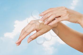 Two woman hands with moisturizer body cream against the sky