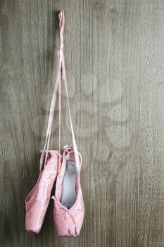 Old used pink ballet shoes hanging on wooden background