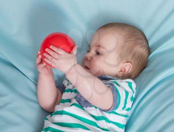 Adorable happy baby boy with red ball on blue background