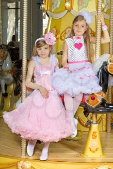 Two beautiful girls in nice lace dresses posing on the carousel