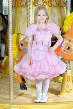 Pretty blond girl in nice pink dress posing on the carousel