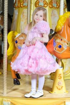 Adorable little girl in pink dress posing on the carousel