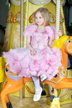 Cute little blond girl in pink dress posing on a carousel pony