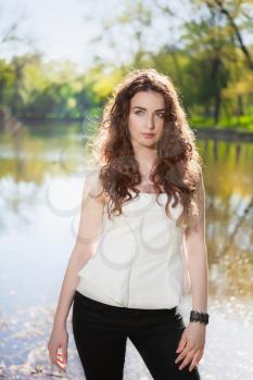 Pretty brunette posing in black pants and white blouse near the pond