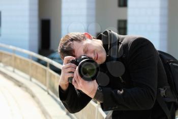Young man in black coat with professional camera taking photograph outdoors