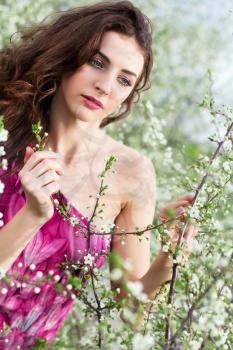 Pretty curly brunette touching the branch of flowering tree