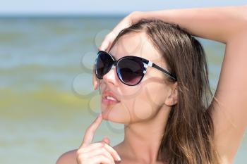 Portrait of sexy woman wearing black sunglasses posing on the beach
