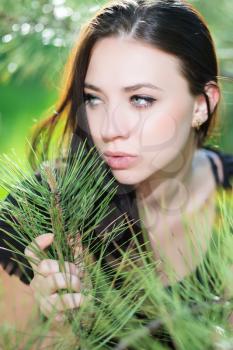 Young thoughtful brunette posing near the pine tree
