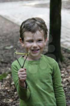Smiling boy with makeshift slingshot in summer forest park