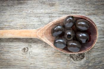 Spoon with black olives on a wooden background