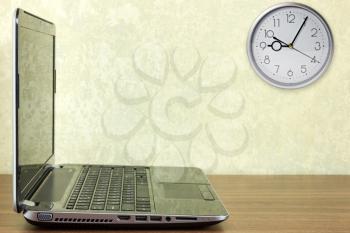Laptop on desk and a business clock on wall