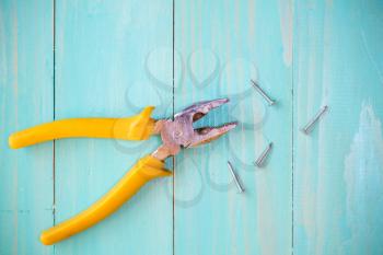 Yellow pliers and few nails on wood background