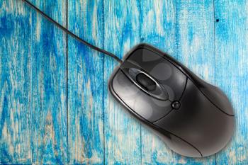 Black computer mouse on the blue wooden planks background