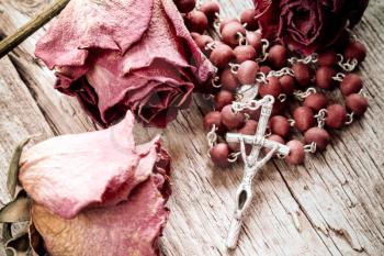 Catholic rosary and faded roses on old wooden background