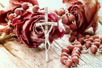 Catholic rosary and dry roses on old wooden background
