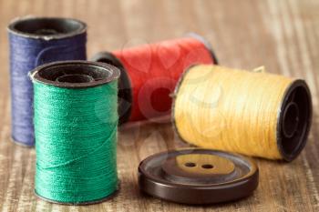 Spools of thread and button on wooden background. 