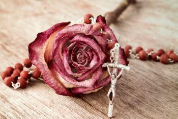 Silver crucifix  and dry rose on wooden background