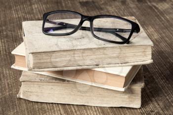Stack of books and reading glasses on the wooden background.